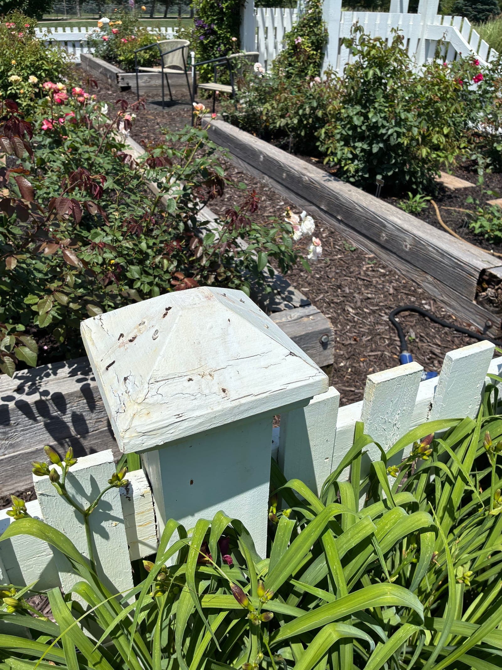 Cracked, weathered wood finial cap on a white picket fence post before replacement
